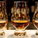 Three glasses of whiskey are sitting on a table.