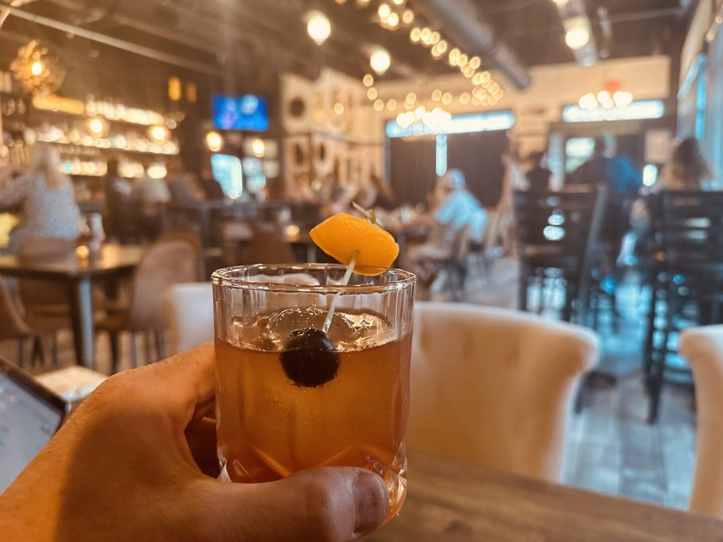 A person holding an old fashioned in a glass.