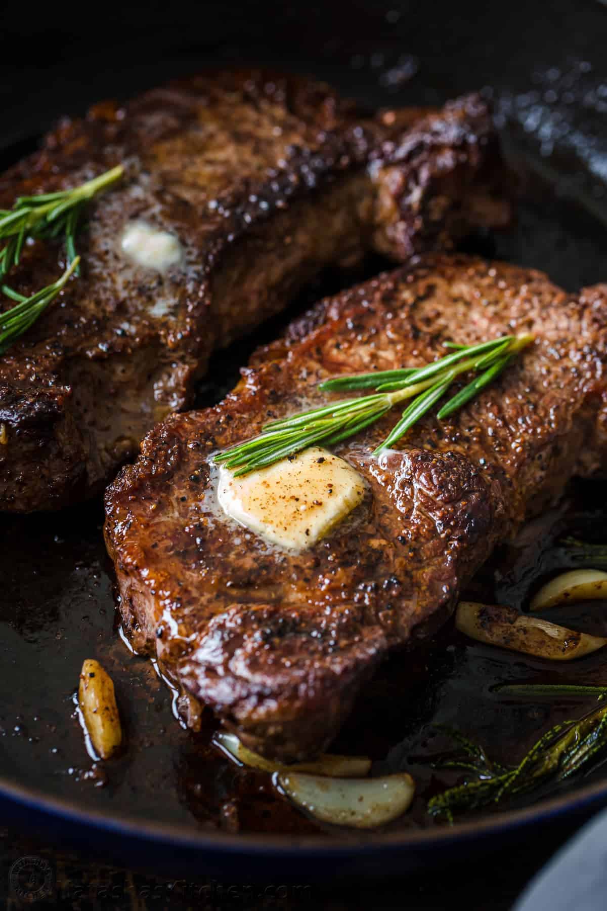 A close up of some steak with butter and rosemary