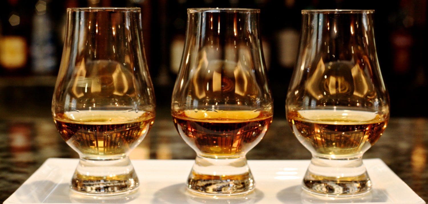 Three glasses of whiskey are sitting on a table.