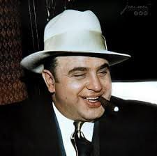 A man in a white hat and suit smoking a cigar.